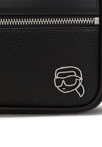 Borsa in pelle nera con superficie texturizzata, zip argentata e un'icona metallica che raffigura un volto con occhiali da sole.