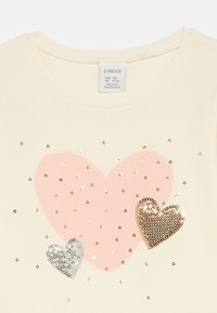 Cream-colored child’s shirt with a large pink heart, smaller silver and gold sequined hearts, and scattered gold sequins on the front.