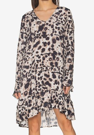 Mujer con un vestido de manga larga y escote en V, con estampado abstracto de animal en negro y beige, y dobladillo asimétrico con volantes.