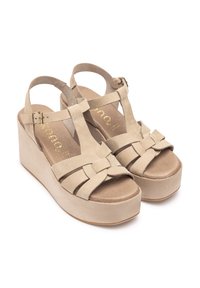Sandali platform beige con tomaia in suede, design a T-strap, dettagli intrecciati e fibbia alla caviglia regolabile. Suola texturizzata per una maggiore aderenza.