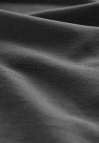 Close-up van donkergrijze stof met zichtbare geweven textuur en zachte plooien die zachte schaduwen creëren.