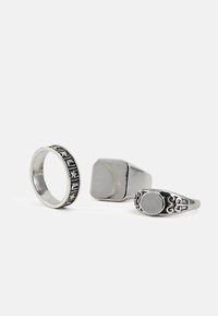 Três anéis de prata: um com texto gravado, um design quadrado chunky e um estilo decorativo com um topo circular. Todos apresentam superfícies polidas.