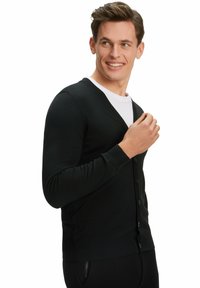 Cardigan nero a maglia con scollatura a V, chiusura con bottoni e polsini a costine. Indossato sopra una camicia bianca, caratterizzata da una vestibilità slim e una superficie liscia.