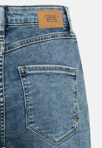 Blauwe denim jeans met een leren label met de tekst "camel active" op de tailleband, voorzien van een achterzak met gedetailleerde stiksels.
