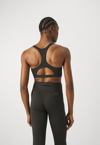 Svart sportsbh med utskåret bakdesign, laget av elastisk materiale. Kombinert med høytlivs svarte leggings, som har en liten lomme.