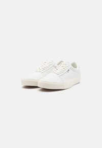 Baskets en toile blanche à coupe basse, avec des panneaux latéraux texturés, des lacets plats et une semelle extérieure en caoutchouc. Détail de marque minimaliste.