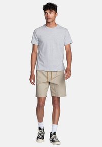 T-shirt en coton gris, design uni ; shorts beiges avec une taille élastique et un cordon de serrage ; portés avec des chaussettes blanches et des baskets montantes noires.