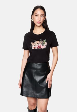 Schwarzes Baumwoll-T-Shirt mit einem gestickten Tigerkopf und floralen Akzenten; kombiniert mit einem schwarzen Lederrock, der eine schlanke Form betont.