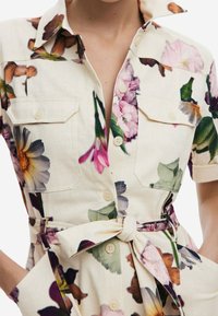 Sukienka koszulowa w kwiatowy wzór, wykonana z lekkiego materiału, z kołnierzykiem, z przodu zapinana na guziki, z dwiema kieszeniami na piersi i pasek w talii.