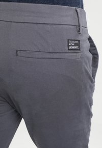 Gray Kiomi pants with a smooth texture, featuring a back pocket and brand label on the right side. Simple design with no patterns.