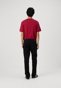 Camiseta roja de manga corta combinada con pantalones negros, con un diseño ajustado. El fondo es liso y claro, centrando la atención en la camiseta.