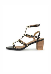 Zwarte sandalen met bandjes, goudkleurige studs, open teen en een medium blokhak. Voorzien van een verstelbare enkelband en een gestructureerde houten hak.
