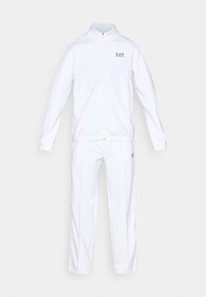 Bela trenirka iz gladkega, lahkega materiala. Jakna ima zadrgo spredaj, visok ovratnik in logotip; hlače imajo elastičen pas in ozek kroj.