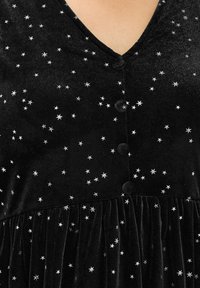 Schwarzes Samtkleid mit V-Ausschnitt, silbernem Sternenmuster und Knopfverschlüssen. Der Rock hat eine geraffte Textur für zusätzliches Volumen.