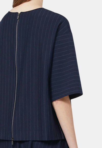 Maglietta a righe blu navy con una vestibilità comoda, maniche corte e una cerniera visibile sulla schiena. La texture del tessuto appare liscia e leggermente strutturata.