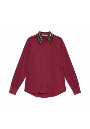 Chemise à manches longues couleur bordeaux avec un col orné de perles noires, dorées et métalliques ; texture douce ; boutonnage avant ; ourlet arrondi.