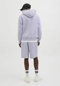 Lila hoodie med en framficka och dragsko, kombinerad med matchande lila shorts och vita sneakers med svart-vita randiga strumpor.