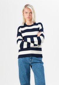 Pulover tricotat striped albastru și crem, cu guler rotund și mâneci lungi, asortat cu o pereche de blugi de denim albastri cu talie înaltă.
