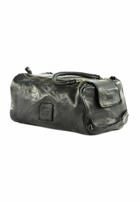 Borsa da viaggio in pelle nera con forma arrotondata, chiusura superiore a zip, manico laterale e patch in rilievo. Texture morbida con leggera lucentezza. Accenti in hardware dorato.