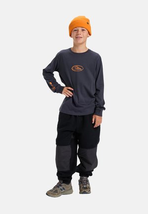 Chemise à manches longues navy avec logo orange, assortie à un pantalon en polaire noir avec des accents gris et des baskets assorties. Bonnet en tricot orange.