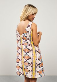 Robe sans manches à motifs géométriques en orange, jaune et bleu sur un fond clair ; dos avec une découpe en forme de V.