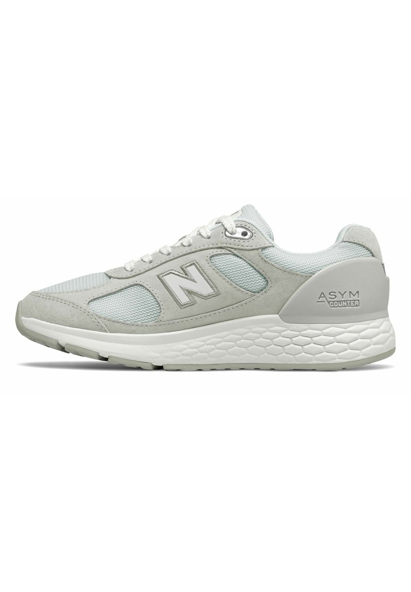 Zapatilla deportiva gris que combina materiales de ante y malla, una entresuela blanca texturizada y un destacado logo 'N' en el lateral.