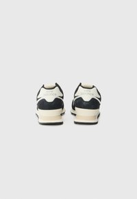 Baskets noires et grises en matière suédée, avec une semelle intermédiaire couleur crème, et le logo "New Balance" sur le talon.