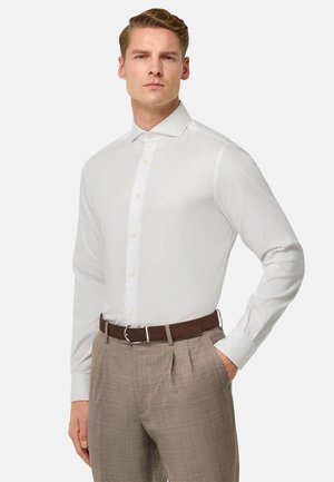 Camicia bianca a maniche lunghe con bottone frontale, dotata di colletto classico. Indossata con una cintura marrone e pantaloni a quadri chiari. Tessuto dalla superficie liscia.