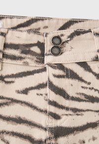 Close-up of beige pants with black zebra stripes, featuring a double button closure at the waistband.