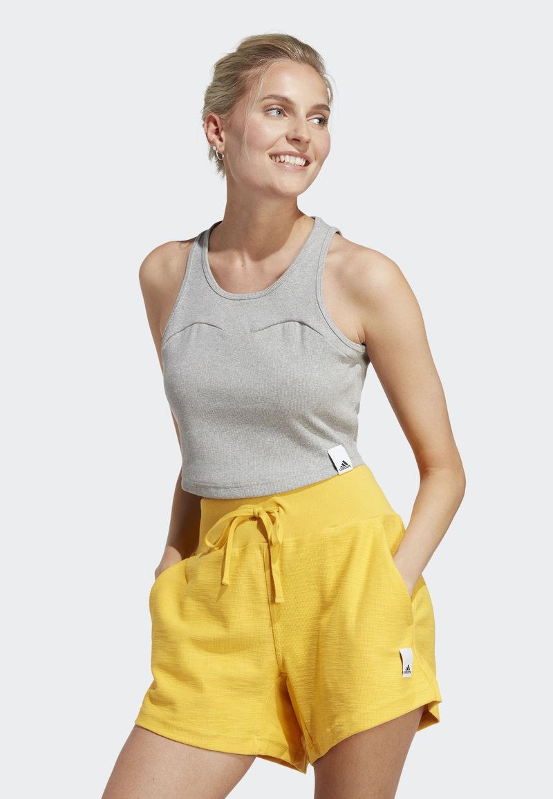 Top corto grigio con texture a costine e scollatura arrotondata, abbinato a pantaloni corti gialli con coulisse e tasche laterali.