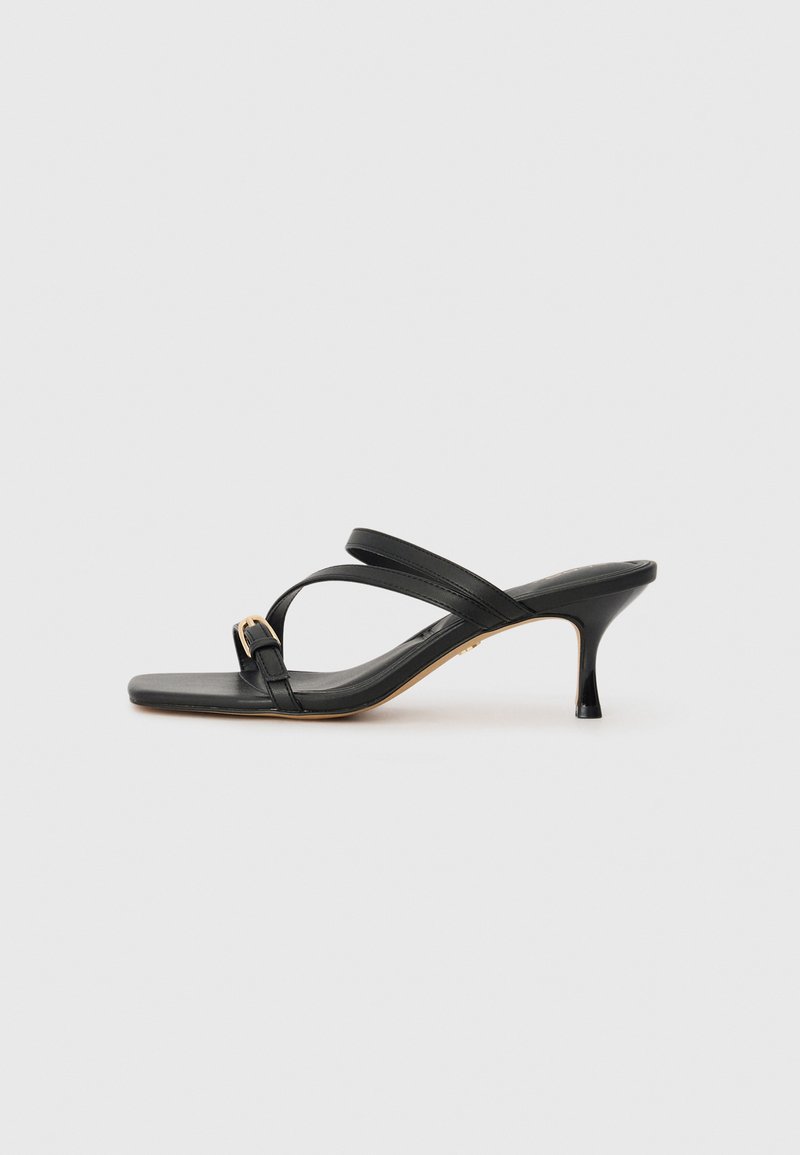Black heeled sandals with a square toe, two crossing straps, gold buckle accent, and a slim high heel. Smooth leather texture.