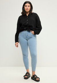 Camisa negra de botones con un acabado texturizado, jeans ajustados de rayas azul claro y sandalias de plataforma negras con una correa ancha.