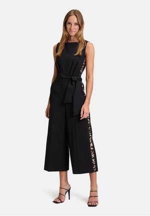 Svart jumpsuit med en figursydd bodice, vida ben och knytbar midja. Sidordelar har ett leopardmönster. Remsandaler fulländar outfiten.