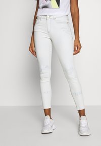 Jeans ajustados de lavado claro con dobladillo desgastado, que cuentan con una tela suave y elástica. Combinados con zapatillas blancas para un contraste.