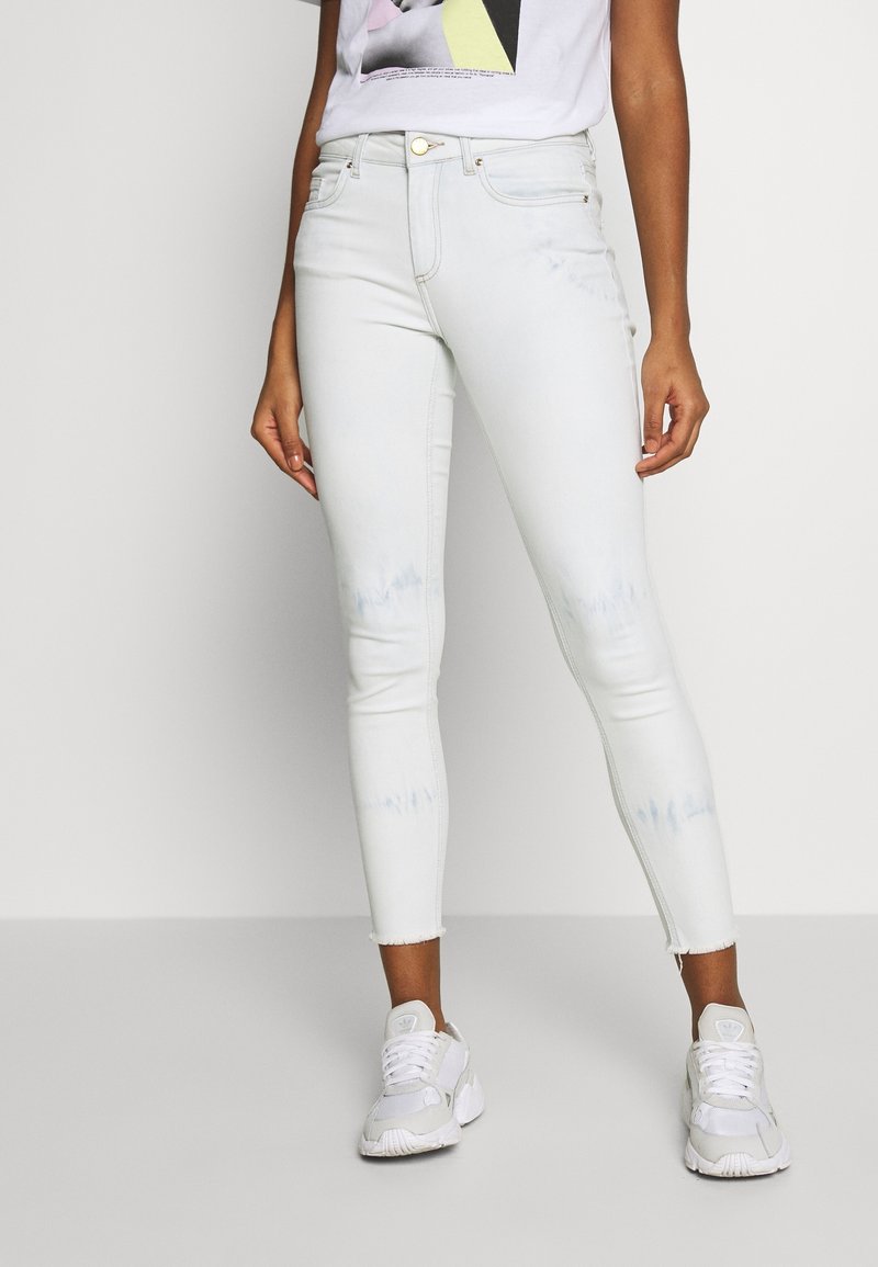 Jeans ajustados de lavado claro con dobladillo desgastado, que cuentan con una tela suave y elástica. Combinados con zapatillas blancas para un contraste.