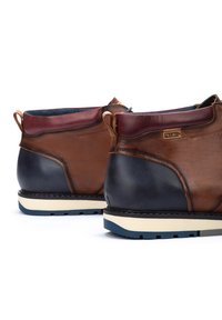 Bruine en marineblauwe leren laarzen met een crèmekleurige middenzool, voorzien van een gestructureerde afwerking, trektabs en contrasterende accenten bij de enkel.