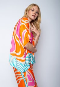 Jasno kolorowa bluzka i dopasowane spodnie wykonane z gładkiego materiału, z wirującymi pomarańczowymi, różowymi i niebieskimi wzorami oraz szerokimi rękawami.