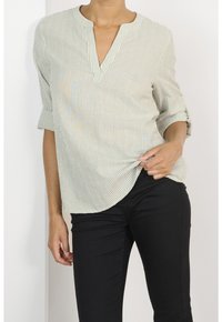 Light green striped blouse with a half-placket, roll-up sleeves, and curved hem. Worn with black pants, featuring a smooth texture.
