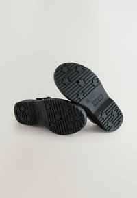 Chaussures en caoutchouc noires avec une semelle texturée arborant des motifs d'étoiles, affichant un design robuste adapté à diverses surfaces.