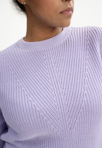 Lavendelfarbener Strickpullover mit geripptem Rundhalsausschnitt und strukturiertem Muster mit vertikalen Linien. Der Stoff wirkt weich und leicht.