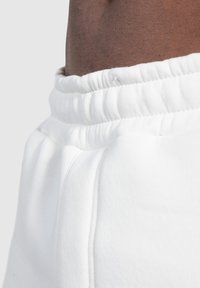 Weiße Sweatpants verfügen über einen gerippten elastischen Bund und eine subtile Textur, mit Seitentaschen und einem Überroll-Detail nahe dem Bund.