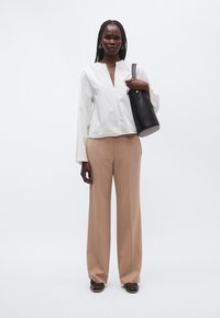 Λευκό πουκάμισο με μακριά μανίκια και V-λαιμόκοψη, σε συνδυασμό με μπεζ παντελόνι φαρδύ στη φάση. Μαύρη δερμάτινη τσάντα τονίζει την εμφάνιση.