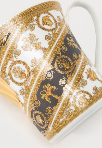 Λευκή πορσελάνινη κούπα με περίτεχνα χρυσά και μαύρα μπαρόκ σχέδια, μεσογειακά μοτίβα και χρυσή λαβή σε απλό φόντο.