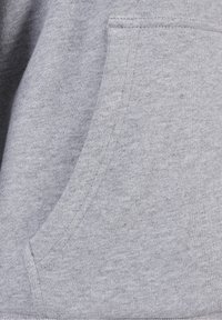 Gros plan d'une poche en tissu gris clair sur un sweat-shirt, montrant la texture et les détails des coutures.