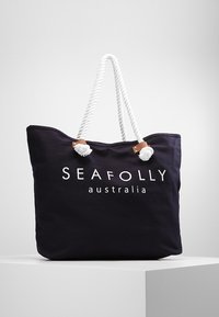 Mörkblå canvas tote-väska med vita repetaxlar, som har en logotyp och texten "SEAFOLLY australia" i vit tryck. Mjuk textur, rymlig design.