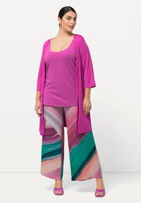 Lyserød top og lang cardigan parret med lange, mønstrede bukser med grønne og lyserøde svulm. Matchende lyserøde sandaler fuldender outfittet.