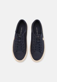 Navy canvas sneakers with round toes, marked with a gold logo, secured by laces, and featuring a textured jute midsole.