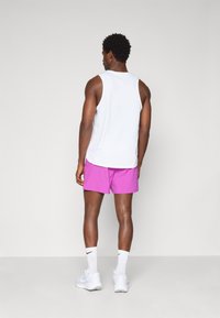 Weißes ärmelloses Athletikshirt und leuchtend pinke Shorts mit lockerer Passform. Kombiniert mit weißen Turnschuhen und Crew-Socken.