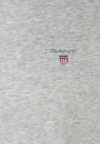 Sudadera gris con una textura suave, con un logotipo de "GANT" bordado y un diseño de escudo en rojo, blanco y azul en el pecho.
