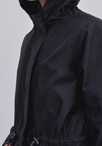 Černá, lehká bunda s kapucí, se zapínáním na zip, elastickými manžetami a stáhnutým pasem. Hladká textura s elegantním designem.